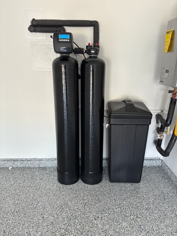 Two black treatment tanks and a brine tank installed in a garage
