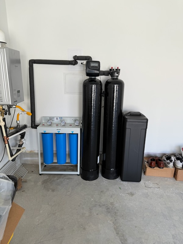 Three blue filters, two black tanks, and a brine tank in a garage